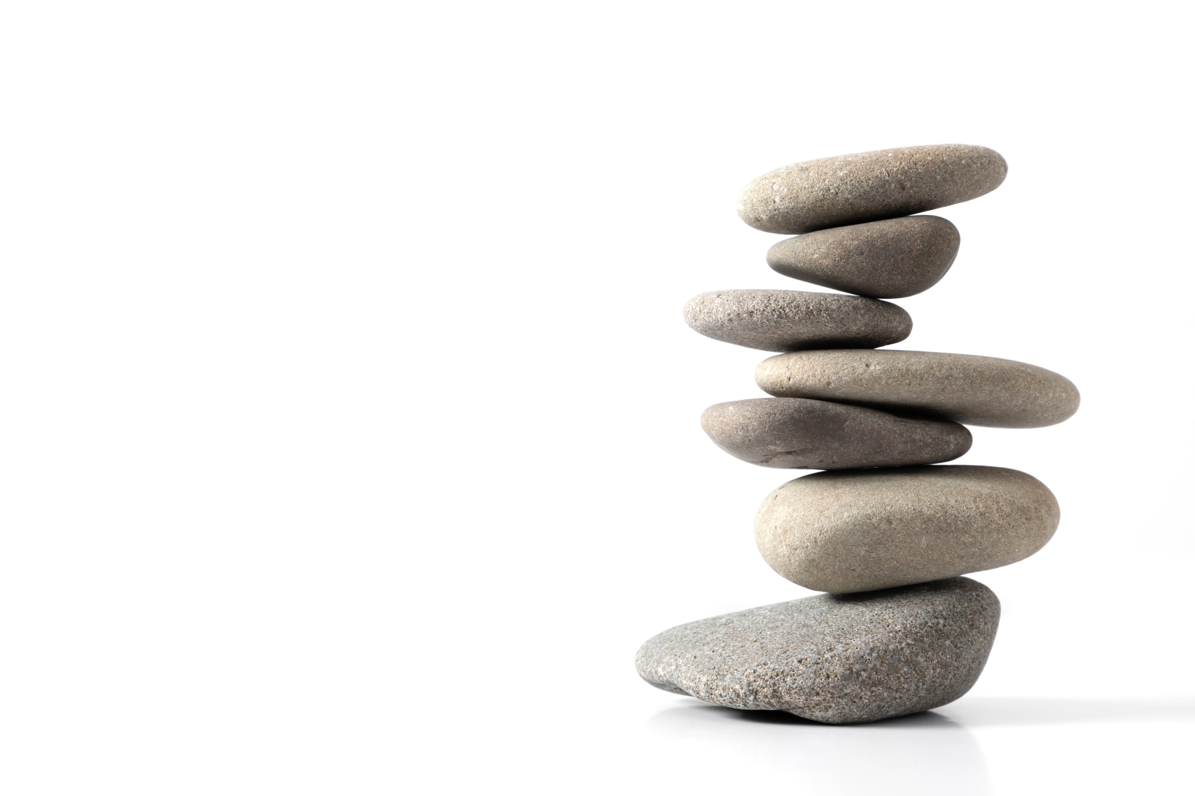 Seven smooth grey river stones stacked in a balanced formation against a solid white background.